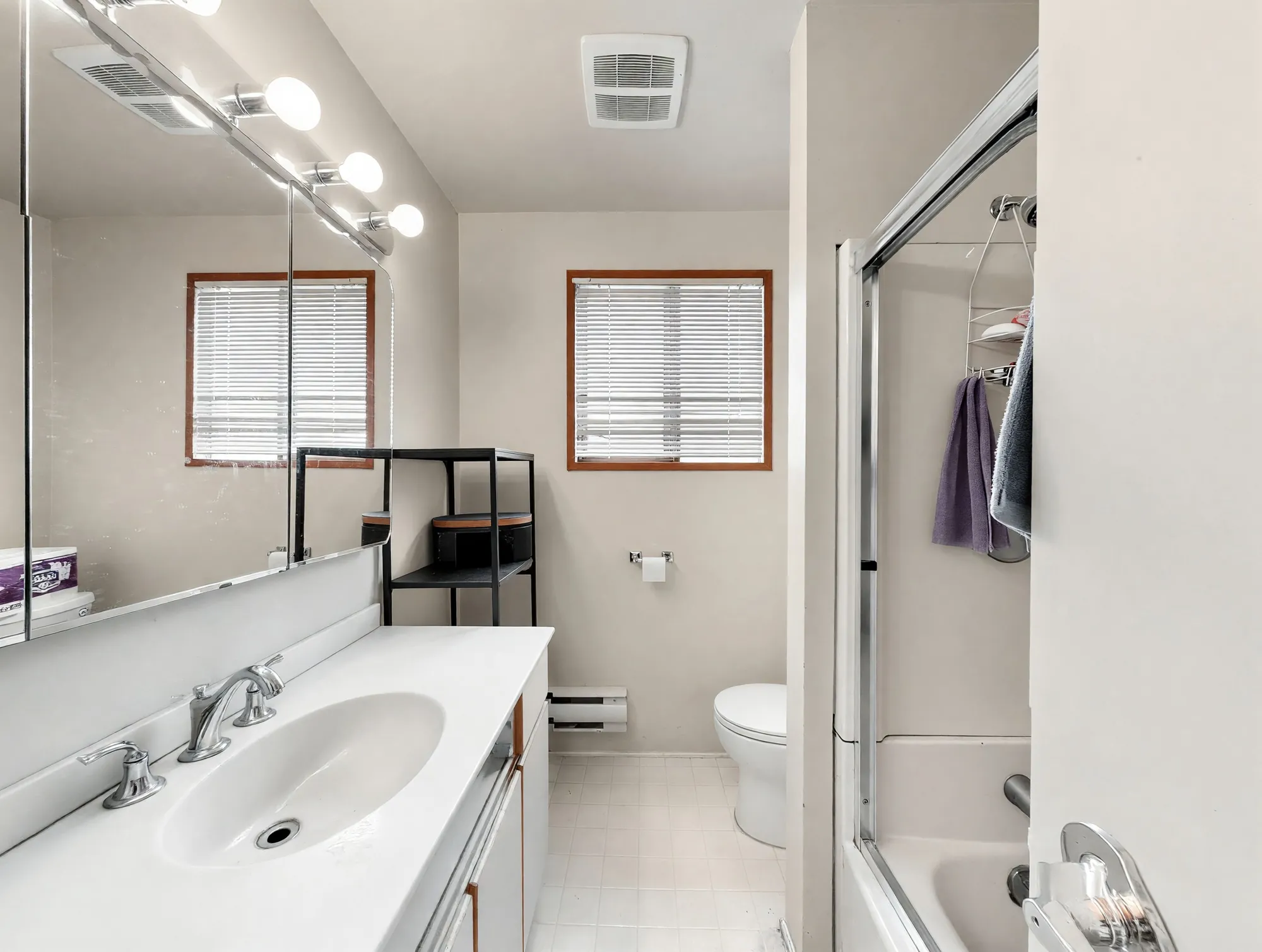 A bathroom with a long vanity, two windows and a tub with a glass shower screen