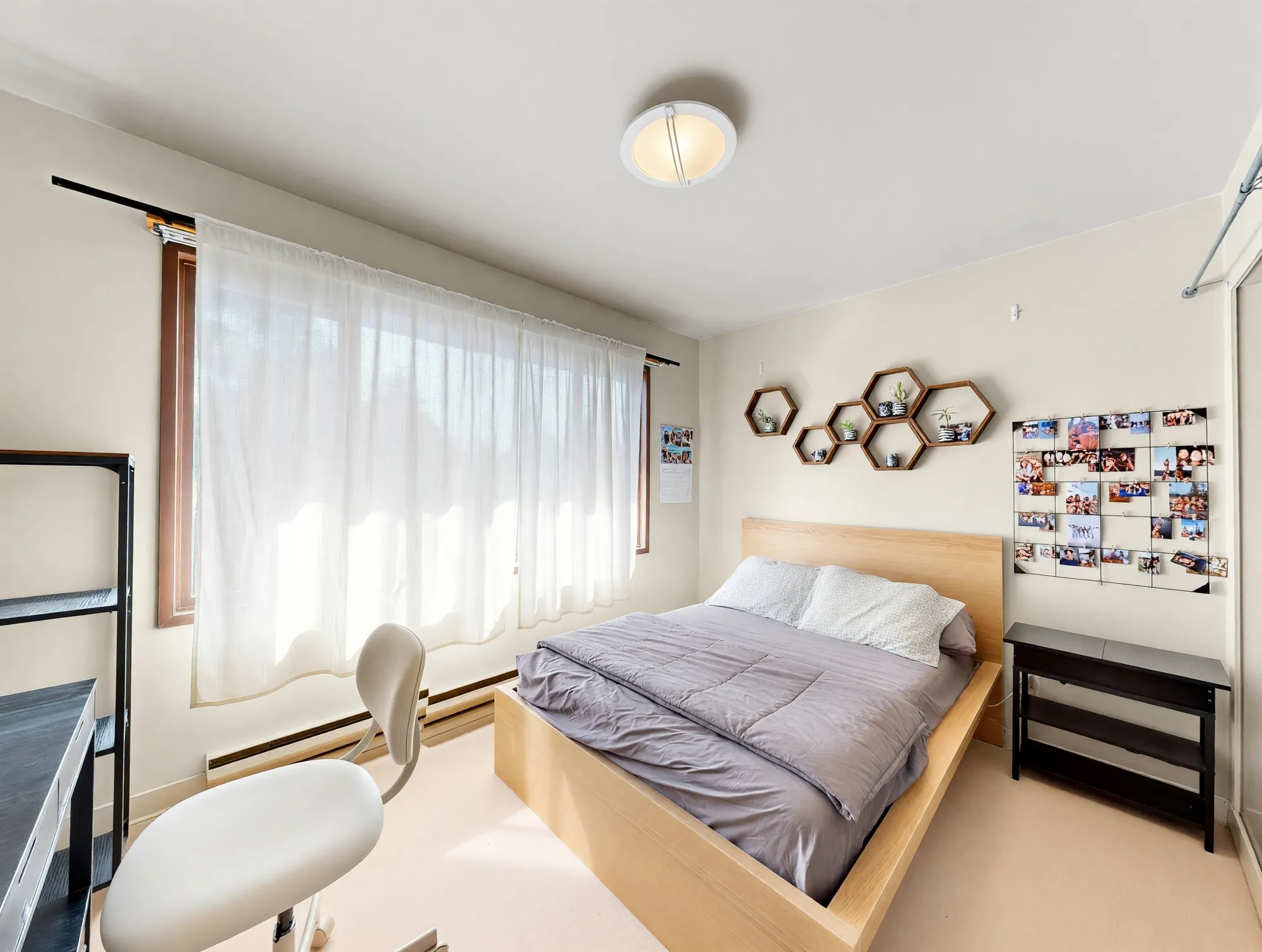 A bedroom with sheer curtains along the window wall and hexagonal shelves