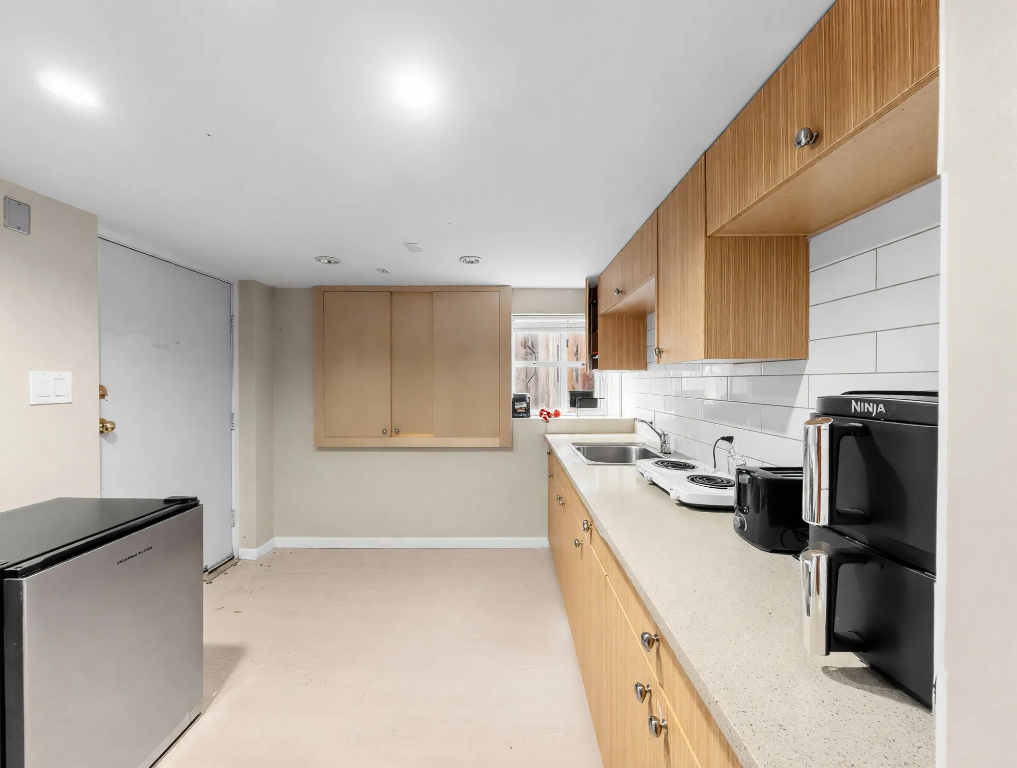 A second, galley kitchen with pale cabinets and a small refrigerator