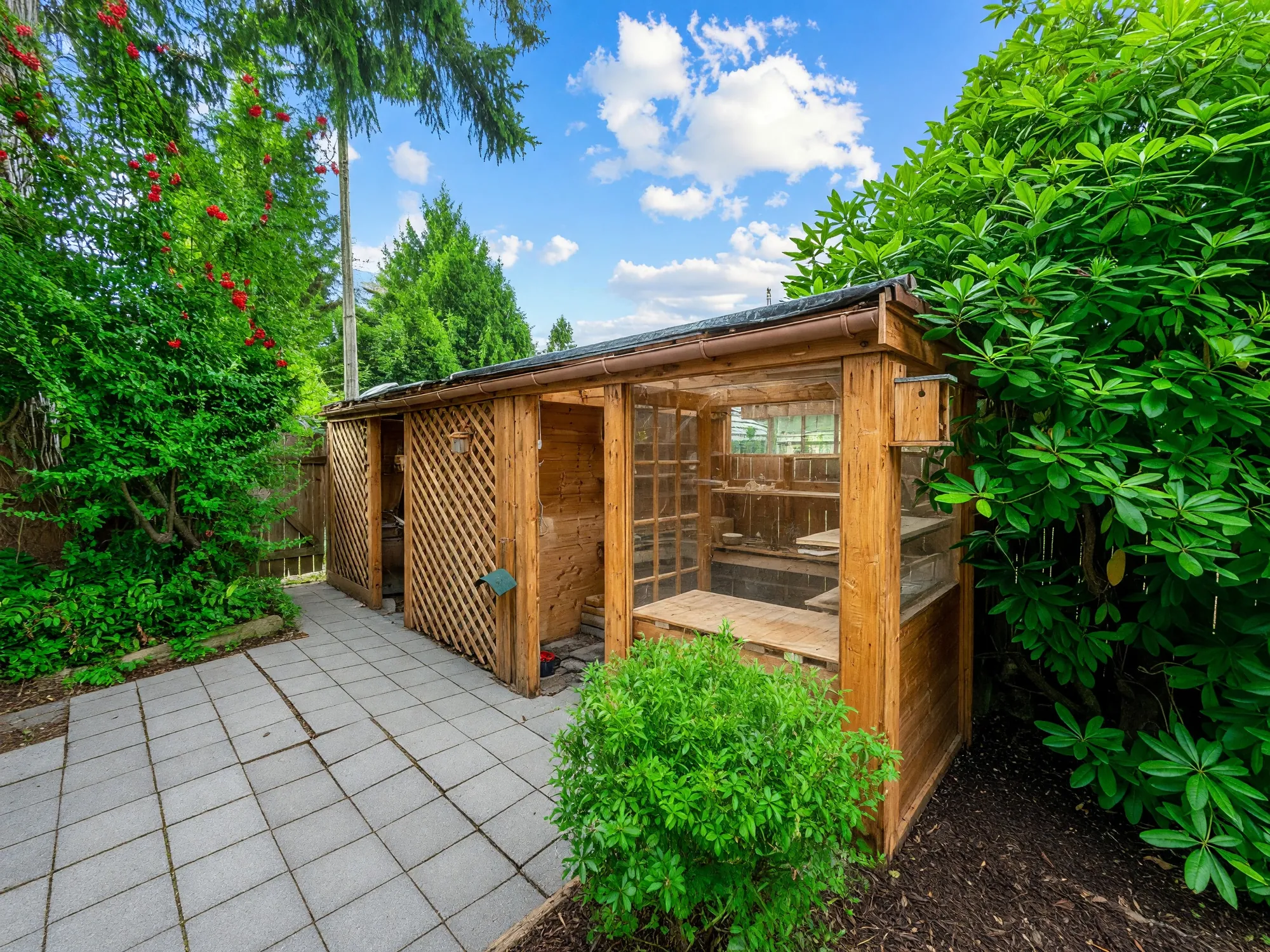 A cedar shed with lattice sides at the lane end of the lot, on a paved apron